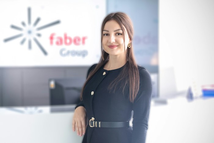 Frau mit langen braunen Haaren steht an einem weißen Tresen mit Logo im Hintergrund