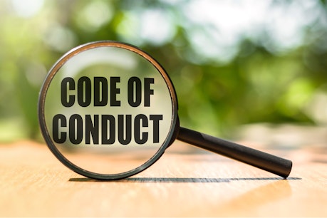 Magnifying glass with text CODE OF CONDUCT on wooden table and green background