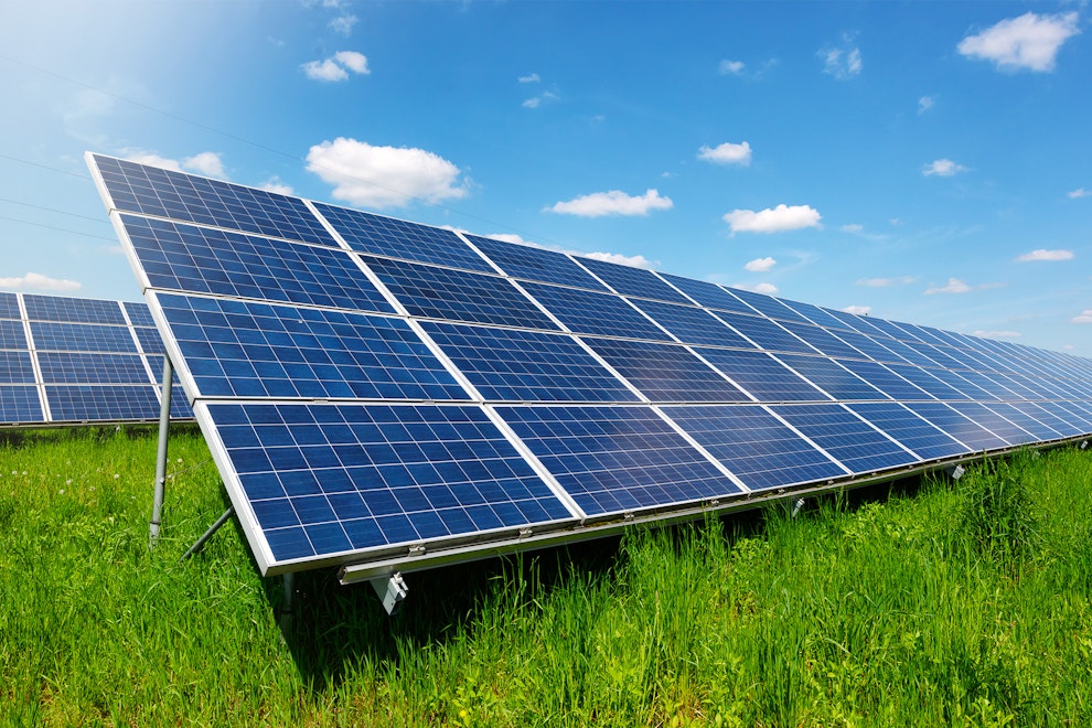 Solar panels on a green meadow with a blue sky and sunshine