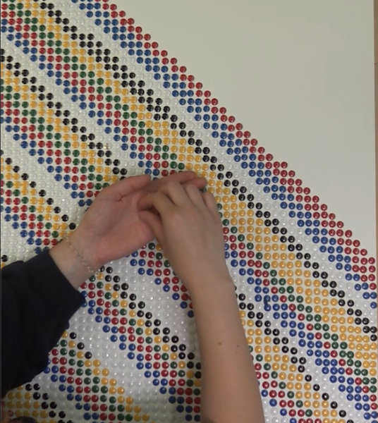 Hände die bunte Reißzwecken auf einer Leinwand befestigen